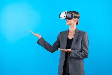 Sanal gerçeklik gözlüklü bir iş kadını mavi arka planda dururken kendine güvenen bir fikirle karşınızda duruyor. Profesyonel proje yöneticisi elinde bir şey tutarken takım elbise giyiyor. Teknoloji. Kısıtlanma.