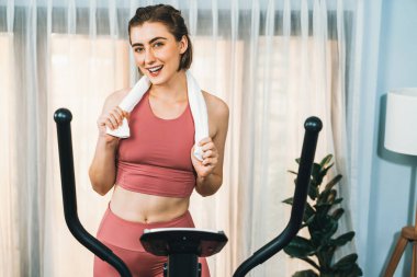Spor ve atletik bir kadın, evdeki fiziğe ve sağlıklı spor yaşam tarzına uygun vücut egzersizi sırasında eliptik koşu makinesiyle koşuyor. Gaiety evde egzersiz eğitimi.