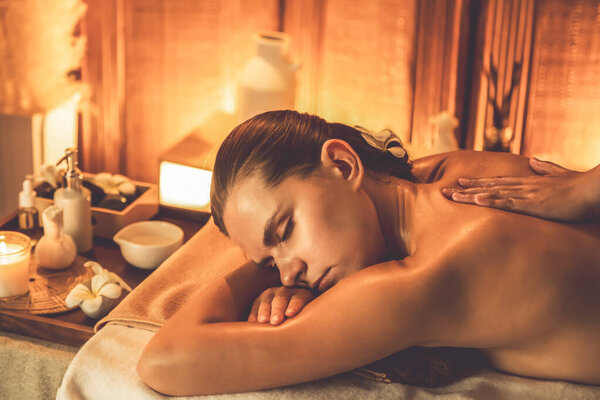 Caucasian woman customer enjoying relaxing anti-stress spa massage and pampering with beauty skin recreation leisure in warm candle lighting ambient salon spa at luxury resort or hotel. Quiescent