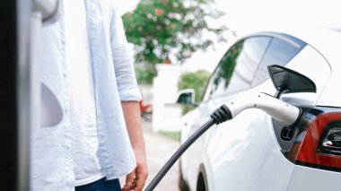 Modern çevre dostu adam EV şarj istasyonundan elektrikli aracı şarj ediyor. EV araba teknolojisi ev sakinleri için gelecekte çevresel sürdürülebilirlik için kullanılıyor. Eşzamanlama