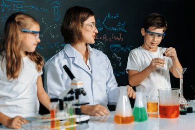 Laboratuvarda çalışan öğretmen, güvenlik gözlüğü takıyor, STEM sınıfında kimya bilimi üzerine deney yapıyor. Öğrenci komedisi tüpte sıvı deneyi yapar. Etkinlik.