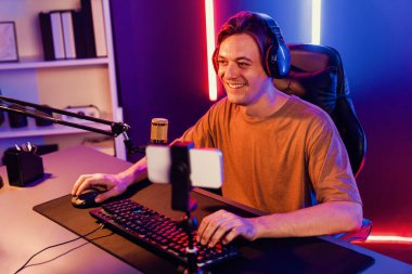 Oyun kanalı, online oyun oynayan akıllı flamalı oyun sunucusu, kulaklık takan, neon ışıklandırma odasındaki takım oyuncusuyla akıllı telefondan canlı yayında konuşan izleyiciler. Bireysel.