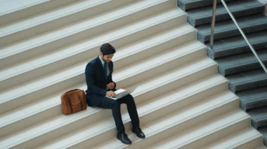 Merdivenlerde dizüstü bilgisayar kullanarak yatırımcıların çalışma ya da planlama stratejisinin en üst görüntüsü. Modern bir otelde dizüstü bilgisayar kullanarak veri analizi yapan takım elbiseli profesyonel bir iş adamı. Sevinçli..