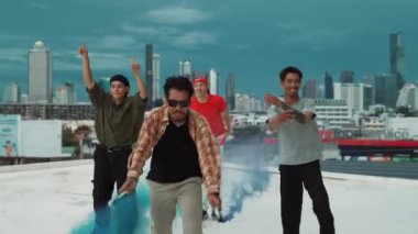 Bir grup çok kültürlü hippi çatıda işaret fişeği çalıyor. Zenci dumanı tutan çekici bir sokak dansçısı hip-hop müzik eşliğinde break dans yapıyor. Açık hava sporu 2024. Sokak dansı. hiphop.