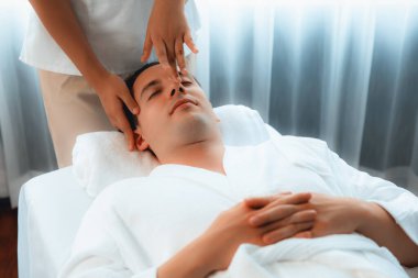 Beyaz adam stres önleyici kafa masajından ve lüks bir tatil beldesi veya otel spa salonundaki modern ışık ortamında yüz güzelliği eğlencelerini şımartmaktan hoşlanıyor. Sessiz.
