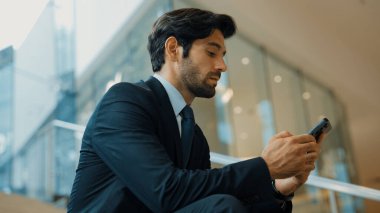 Akıllı proje yöneticisi merdivenlerde otururken cep telefonuna bakıyor. Çekici Kafkasyalı iş adamı telefon kullanarak çalışıyor. Profesyonel yatırımcı iş stratejisi planlamak için telefonu kullanıyor. Sevinçli..