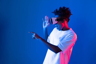 Sanal gerçeklik dünyasını dijital fütüristik teknolojiye bağlayan mavi pembe ışık duvarını gösteren 3 boyutlu hologram gösteren genç bir Afro-Amerikan oyun oyuncusu. Entrika.