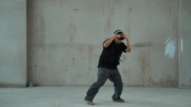Kulaklıktan çimento arka planda müzik dinlerken break dans pratiği yapan yakışıklı bir hippi. Sokak dansçısının hareketli çekimi robot dansı yapar. Açık hava sporu 2024. Modern dans. hiphop.