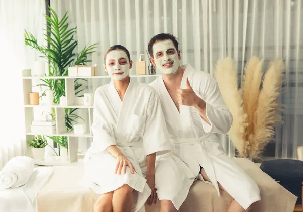 stock image Blissful couple in bathrobe with facial cream mask enjoying serene ambiance of spa salon resort or hotel during holiday. Pampering face spa and skincare treatment with essence relaxation. Quiescent