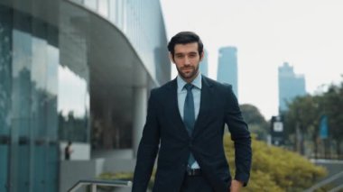 Profesyonel iş adamı hareket ediyor ve kameraya bakarken ayakta duruyor. Gülümseyen yönetici kameraya kendinden emin bir şekilde gülümsüyor. Mimari binada takım elbiseli yatırımcıların yakın çekimi. Sevinçli..