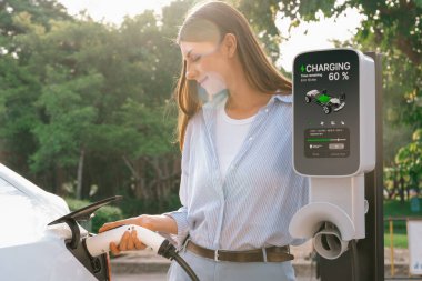 Yolculuk sırasında doğal ormanlarda ya da güneş ışığı alan ulusal parklarda elektrikli araba için şarj olan genç bir kadın. Tatil ve tatil boyunca çevre dostu seyahat. Yükselt