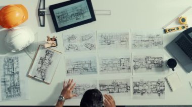Proje planını kontrol ederken ve seçerken mimar mühendisin bina planlarını masaya yerleştirdiği tepeden aşağı hava görüntüsü. İç mimar toplantı masasından mimari plan seçti. Hizalama.
