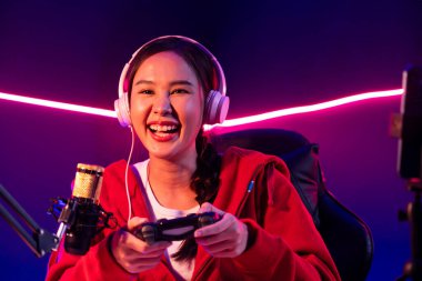 Oyun çubuğu ile gülümseyen Asyalı güzel kız flamasının sunucu kanalı kulaklık yapıştırıcısı takarak online izleyici medyasıyla konuşuyor. Esport yetenekli takım oyuncuları neon odada. Taktik.