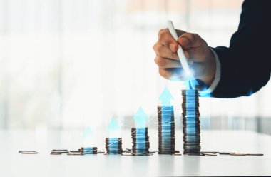 Dijital grafik göstergeli bozuk para yığını iş yatırımını ve ekonomik büyümeyi sembolize ediyor. Finansal hedefe ulaşmak ve kâr sağlamak için finansal planlama yapan bir iş adamı. Kurnaz.