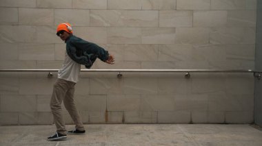 Asyalı akıllı hipster, kulaklık ve şık kıyafetler giyip hip hop şarkıları dinlerken gri arka planlı enerjik break dans gösterisi yapıyor. Açık hava sporu 2024. Hip hop hareketi. Yumuşak bir şekilde..