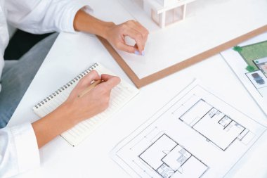 Asyalı kooperatif iş arkadaşı ev modelini ev modeliyle ve bina planıyla birlikte masaya koyarken, profesyonel güzel mimarın el yapımı taslaklarının en üst görüntüsü. Tertemiz..