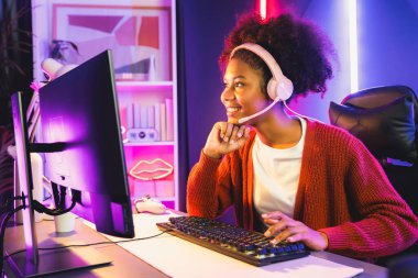 Neon renkli aydınlatma odasında kulaklık takan Afrika kökenli Amerikalı kız flamalı Esport yetenekli takımıyla online dövüş yapıyor. Rakiplerini kazanmak için strateji planlayan diğer oyuncularla konuşmak. Tatlandırıcı.