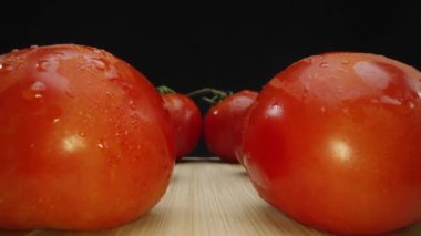 Kesme tahtasındaki siyah arkaplanlı taze domatesi yakın plan. Sulu kırmızı bir domates, iyi giyilmiş bir ahşap kesme tahtasının üzerinde gururla oturur. Taze domates, kıpkırmızı etini ortaya çıkarır. Geliştirilebilir.