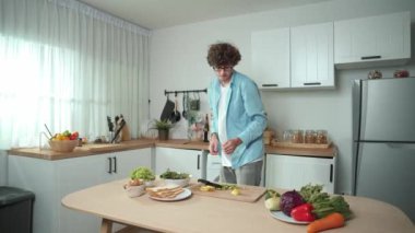 Mutlu baba yemek pişirirken müziğe geçiyor ve modern mutfakta öğle yemeği hazırlıyor. Aktif baba, sebze ve mutfak gereçleri ile çevrili sağlıklı yemek ya da salata yaparken şarkıyla dans ediyor. Pedagoji.