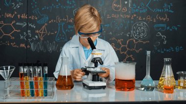 Akıllı çocuk BTMM bilim sınıfında ya da kimya dersinde mikroskop analiz numunesi kullanıyor. Kafkasyalı mutlu öğrenci tüplerdeki kimyasal sıvıyı incelemek için mercek altına bakıyor. Etkinlik.