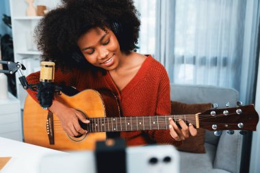 Güzel Afrikalı Kadın Etkilenen 'in sunucu kanalı akıllı telefondaki yayın stüdyosunda gitar çalarak şarkı söylüyor. Canlı sosyal medyada müzik blogcusu zamanı. Ses yaratıcısı kavramı. Tatlandırıcı.