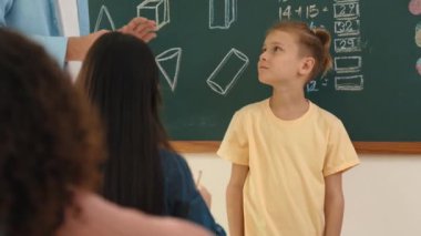 Profesyonel öğretmen konuşuyor ve sınıfta Asyalı çocuğa fikrini açıklıyor. Sınıfın önünde karatahta matematik dersiyle dikilmiş beyaz öğrenci dinleme eğitmeni. Pedagoji.