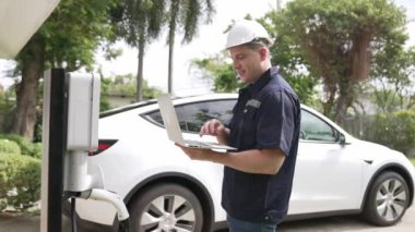 Evde EV şarj istasyonu kurulumu üzerinde çalışan nitelikli teknisyen, EV için dizüstü bilgisayarla şarj sisteminde sorun çıkarma ve yapılandırma ayarları yapıyor. Titiz