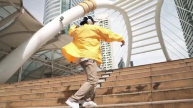 Asyalı şık bir adam alçak açılı kamerayla hip hop dansı yapıyor. Break dansçı, şehirde kulaklıktan müzik dinleyip dans ederken merdivenlerden çıkıyor. Açık hava sporu 2024. Yumuşak bir şekilde..