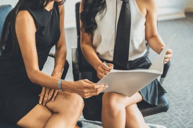 İki iş kadını ellerinde mali verilere bakarken iş konuşuyorlar. Ofis toplantı odasındaki sandalyelerde oturuyorlar. uds