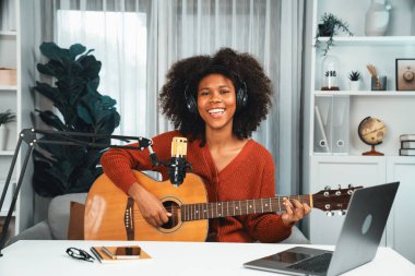 Genç Afrikalı Amerikalı müzisyenin sunucu kanalı gitar çalıyor, şarkı söylüyor, stüdyoda dizüstü bilgisayardan yayın yapıyor. Kulaklık dekorasyonu ve mikrofon kaydı. Tatlandırıcı.