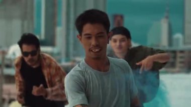 Bir grup çok kültürlü hippi çatıda işaret fişeği çalıyor. Zenci dumanı tutan çekici bir sokak dansçısı hip-hop müzik eşliğinde break dans yapıyor. Açık hava sporu 2024. Sokak dansı. hiphop.