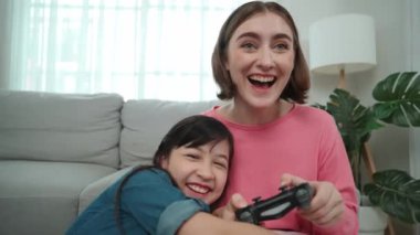 Kafkasyalı bir anne çocuğuna bakıp oyun hakkında konuşurken, mutlu bir kız çocuğu annesinin yanında oturup oyunu kazanıyor. Sevimli kız joystick 'i tut ve başarısını kutla. Pedagoji.