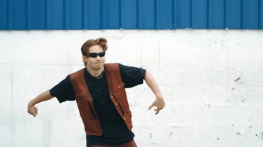 Beyaz arka planda break dans pratiği yapan yakışıklı bir sokak dansçısı. Hip hop tarzı giyinen sporcu, mavi arka planlı bir sokakta müzik eşliğinde ayak sesleri çıkarıyor. Açık hava sporu 2024. ÇalışmaComment.