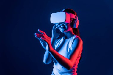 Çevresi siberpunk neon ışıklarıyla çevrili zeki bir kadın metaevrene bağlı VR kulaklık takıyor, gelecekçi siber uzay topluluğu teknolojisi. Sanal objeye el ile dokunan kadın. Halüsinasyon.