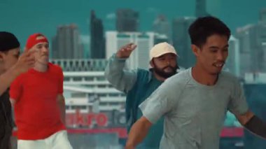 Bir grup çok kültürlü hippi çatıda işaret fişeği çalıyor. Zenci dumanı tutan çekici bir sokak dansçısı hip-hop müzik eşliğinde break dans yapıyor. Açık hava sporu 2024. Sokak dansı. hiphop.