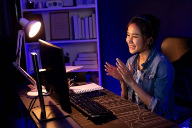 Sunucu kanalı Asyalı etkileyicisi canlı yayında konuşuyor. Sosyal medyada kulaklık takıyor, bilgisayar kaydı yapıyor, dinleyicileri selamlıyor ve Neon Modern Stüdyoları 'nda online olarak koçluk yapıyor. Taktik.