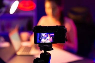 Güzel Asyalı bir kanalın sunucusundaki seçici odak kamera ekranı dinleyiciyle sosyal medyada müzik dinliyor, bulanık arka planda mikrofon kullanarak pastel kulaklık takıyor. Taktik.