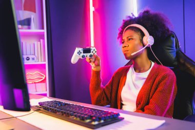 Afro-Amerikalı kız flaması, neon odada kulaklık takarak Esport yetenekli takımıyla online dövüş yaparken hayal kırıklığına uğradı. Rakiplerini kazanmak için strateji planlayan diğer oyuncularla konuşmak. Tatlandırıcı.