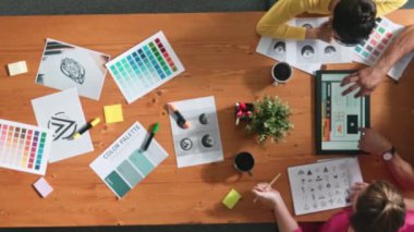 Proje yöneticisi renk paletleri seçerken tasarımcının tablete baktığı yukarıdan aşağıya hava görüntüsü. Profesyonel grafik tasarımının en üst görüntüsü ve logoya bakın. Yetenekli ekip grafikleri seçiyor. Sempozyum.