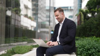 Yeşil Şehir 'deki akıllı proje yöneticisine rapor yazmak için dizüstü bilgisayarı üzerinde çalışıyor. İş adamı analiz verilerine ve beyin fırtınası fikrine bankta otururken bilgisayar kullanarak bakıyor. Urbane.