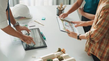 Akıllı iş adamlarının tasarımı planlamak için tabletten proje planına bakarken ve planlar ve toplantı masasındaki bina inşaatı hakkında tartışırken birlikte çalışması. Hizalama.