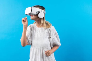 Kız çiçeğin kokusunu alırken mavi arka planda sanal gerçeklik gözlüğü takıyor. VR gözlüklü mutlu kadın görsel gerçeklik dünyasıyla bağlantı kurarken doğa hologramının keyfini çıkar. Teknoloji yeniliği. Kısıtlanma.