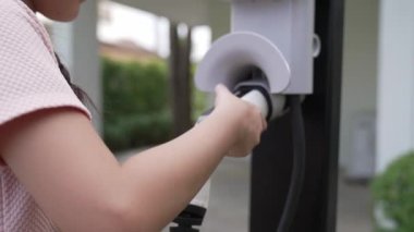 Küçük mutlu kız, EV şarj istasyonundan elektrikli aracı şarj ederken çevre dostu ve enerji sürdürülebilirliğini öğreniyor. EV araba ve sürdürülebilir gelecek nesil konsepti. Titiz