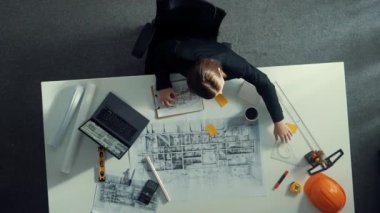 Dizüstü bilgisayarda çalışırken mimari çizimlerin hava görüntüsü. Kafkasyalı mühendisin bina modelini tasarlayıp, ekipman ve güvenlik kaskıyla birlikte tasarladığına dair tepeden aşağı bir bakış açısı. Hizalama.