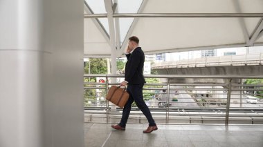 Zeki beyaz iş adamı iş yerine yürürken finansal strateji planlaması için meslektaşını arıyor. Yöneticinin pazarlama ekibiyle iletişim kurmak için cep telefonunu kullanışının yan görüntüsü. Yaşam tarzı. Urbane.