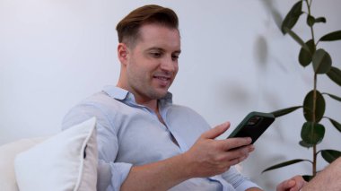 Orta yaşlı bir adam oturma odasındaki koltukta oturur telefon arama verilerini kullanır çocukları iyi bir yetişkin baba ya da eğlence olarak yetiştirir. İşadamı teknolojiyi kolaylık için kullanır. Uyumsuzluk.