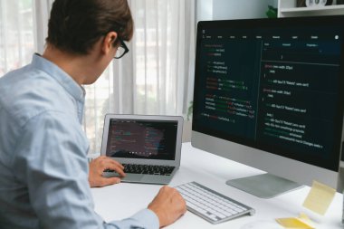 BT geliştiricisi, laptop üzerindeki yazılım geliştirme bilgisi üzerinde çalışırken pc ekran ile karşılaştırma yaparak sürüm uygulaması projesini güncellemek için yeni bir kod programı yaratıyor. Bireysel.