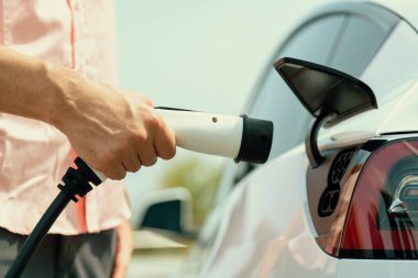 Dışarıdaki şarj istasyonundan EV şarj aletini şarj etmek için elektrikli araca elle tak. Alternatif temiz ve sürdürülebilir enerji kavramına sahip taze gün ışığı ortamı. Kalıcı