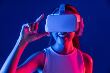 Etrafı neon ışıklı kulaklıklarla çevrili bir kadın metaevreni bağlayan VR kulaklık takıyor, fütüristik siber uzay topluluk teknolojisi yayıyor, işaret ve başparmak ile sanal nesne etkileşimi kuruyor. Halüsinasyon.