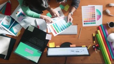 Tasarımcı yazma fikri ekrana bakarken proje yöneticisinin üst görünümü. Akıllı iş adamlarını kapat ve tasarımcı palete bakarken logo tasarımı fikrini açıkla. Sempozyum.